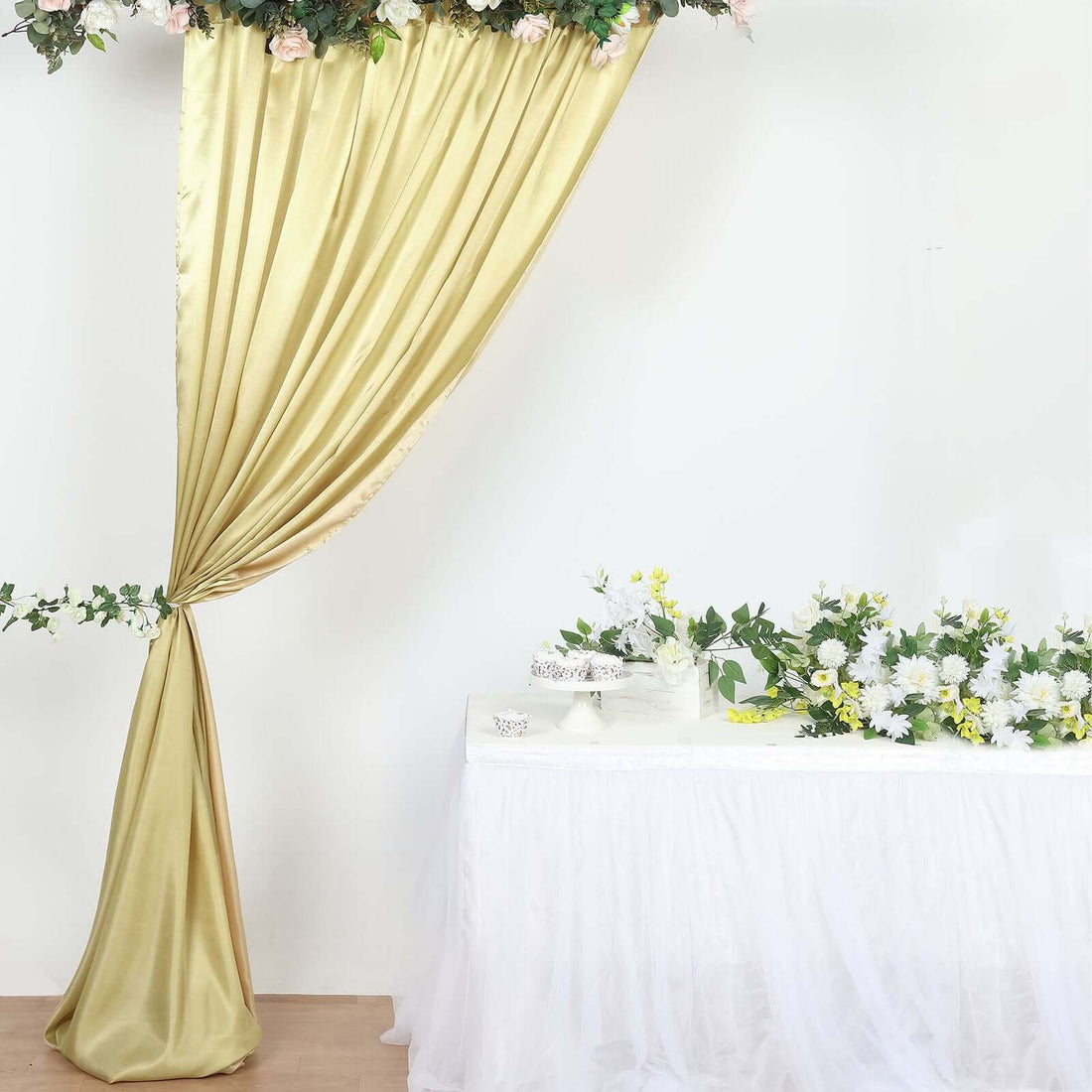Elegant gold curtain with floral accents draped beside a white table adorned with flowers.