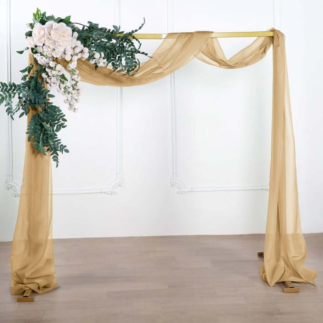 Elegant wedding arch draped with sheer fabric and floral arrangement.