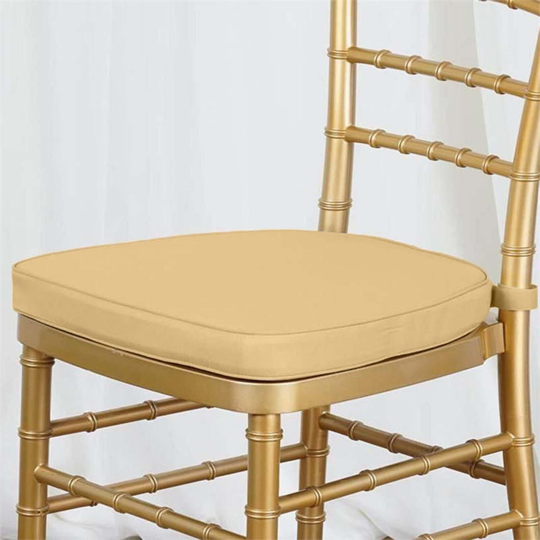 Gold chiavari chair with a beige cushion on a plain background.