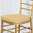 Gold chiavari chair with a beige cushion on a plain background.