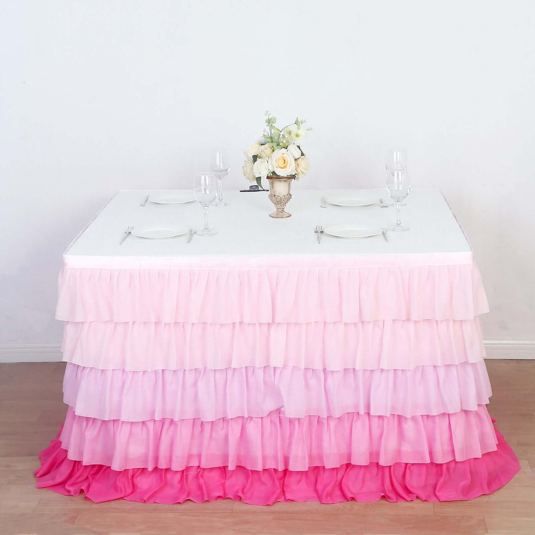 Pink ombre ruffled table skirt with a floral centerpiece and glassware.