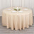 Round beige tablecloth draped over a table with decorative plates and candles.