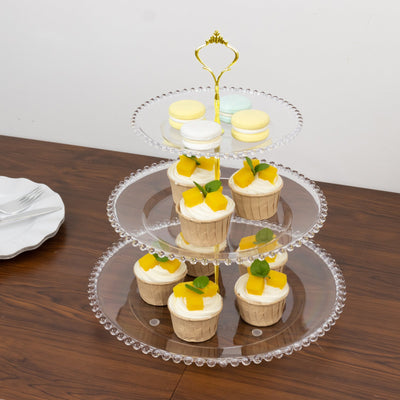 Three-tiered dessert stand with cupcakes and macarons on a wooden table.