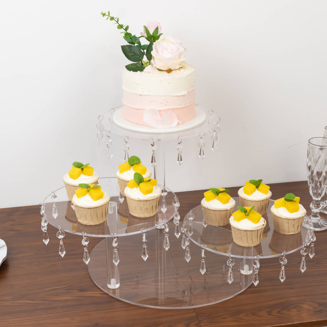 Clear acrylic cupcake stand with cupcakes and a cake, elegantly decorated with flowers.