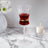 Elegant glass with red drink, gold band and candle on marble surface.