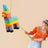 Colorful unicorn piñata being hit by a blindfolded player at a party.