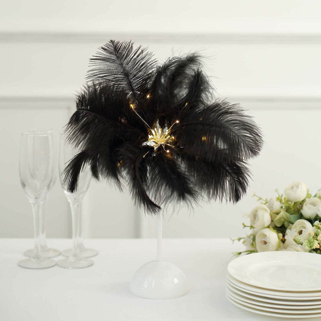 Black feather centerpiece with lights on a white pedestal, elegant table setting.