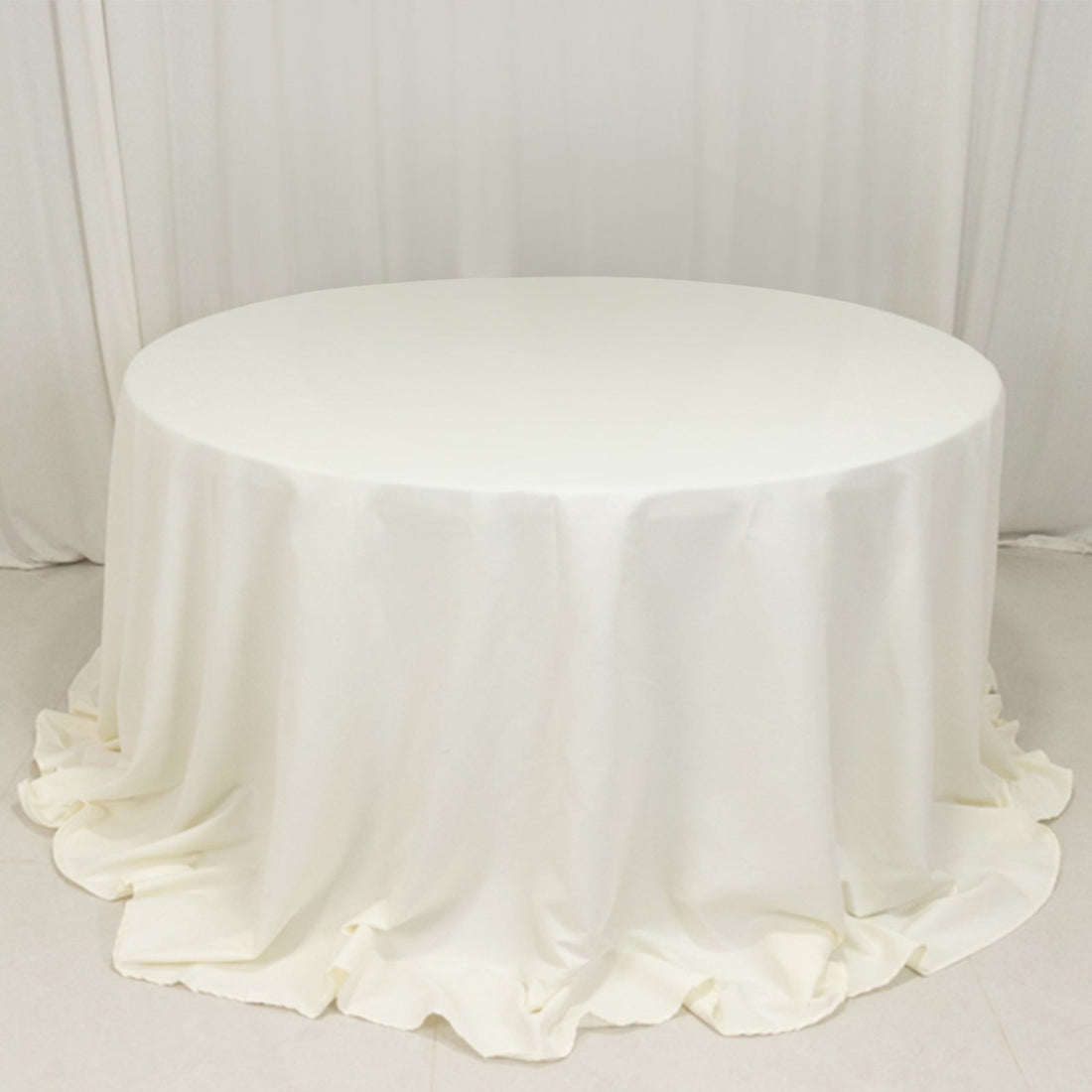 White round table covered with a draped tablecloth.