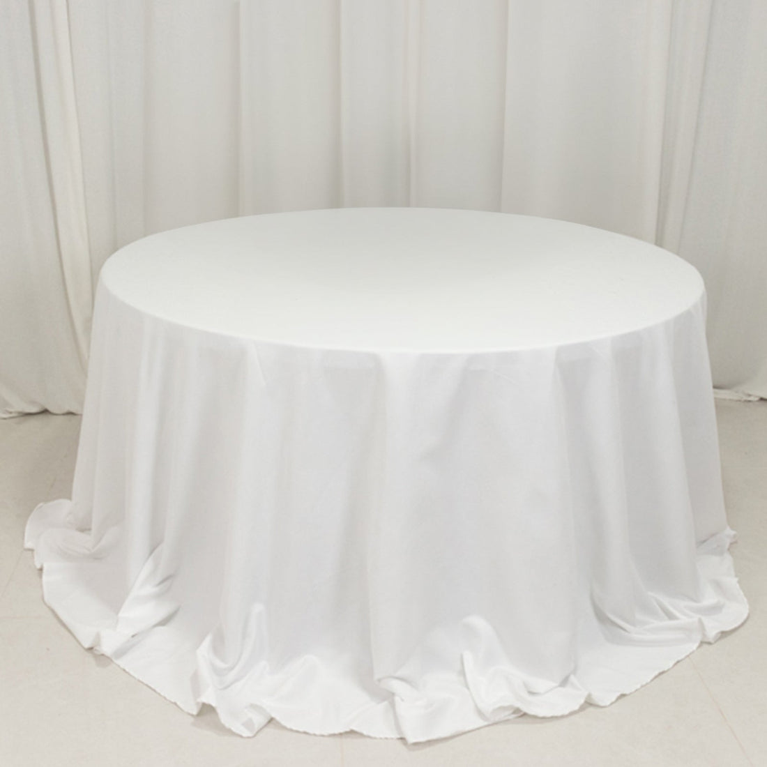 Round white table with a draped tablecloth in a studio setting.