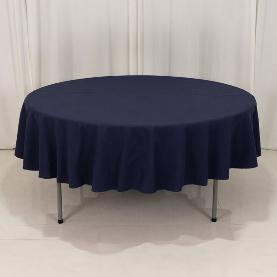 Navy round tablecloth draped on a table with a seamless backdrop.