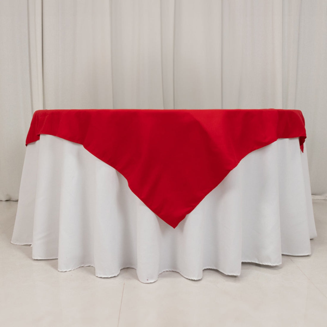 Red tablecloth draped over a white table in a studio setting.