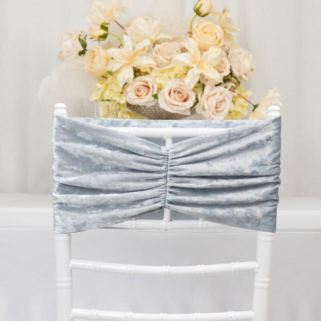 Silver velvet chair sash draped on a white chair with flowers in the background.