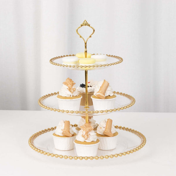 Gold three-tier cupcake stand with decorated cupcakes on a neutral background.