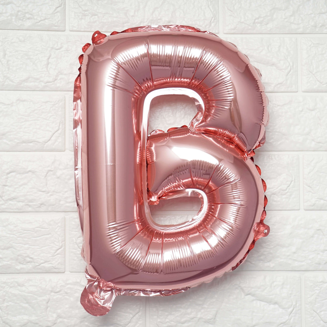 Rose gold foil letter B balloon on a textured white background.