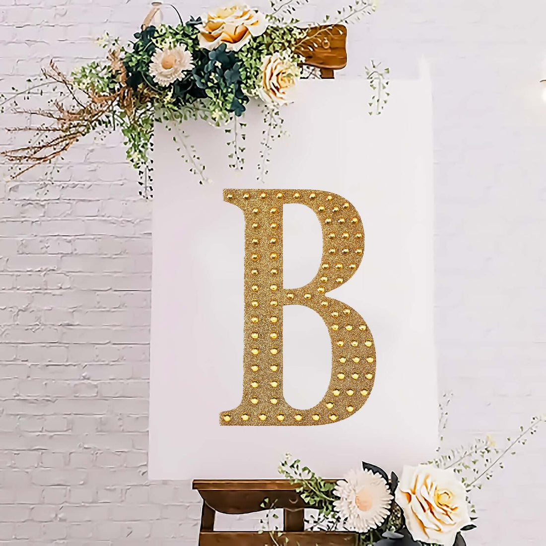 Gold glitter letter "B" on a decorated canvas with flowers.