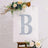 Glittery letter B on an easel surrounded by flowers in a stylish setting.