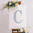 Glittery letter "C" on a decorated canvas with flowers and greenery.