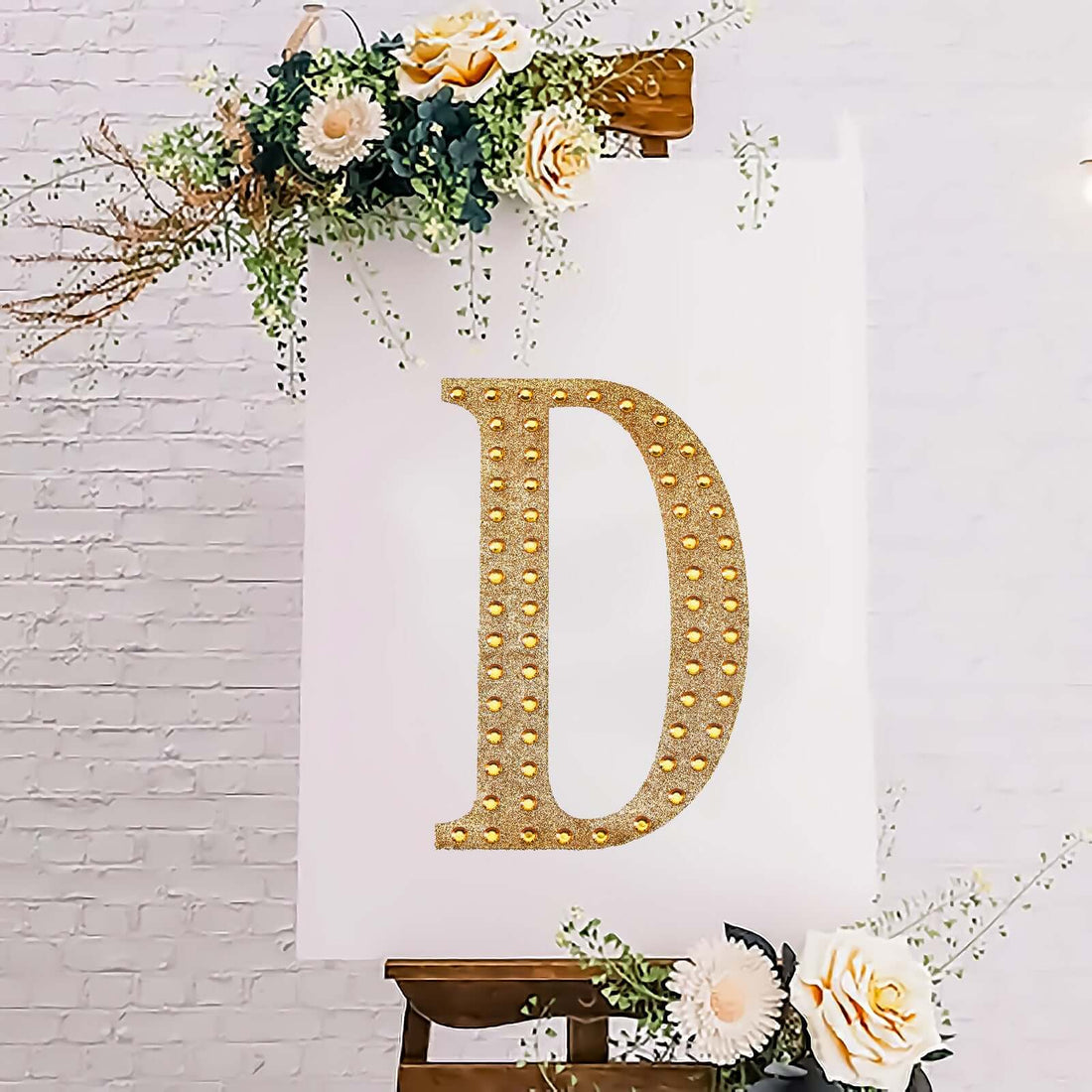 Decorative letter "D" with lights on an easel, adorned with flowers.