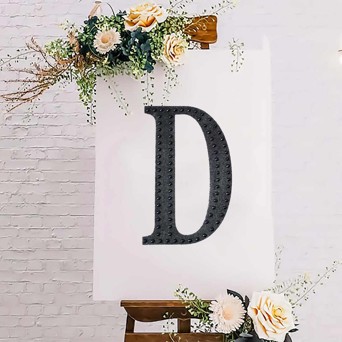 Decorative letter "D" on an easel with floral accents.