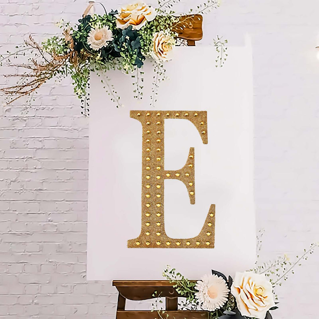 Glittery gold letter "E" on a decorative display with flowers.