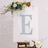 Decorative letter E on a canvas with flowers and greenery.