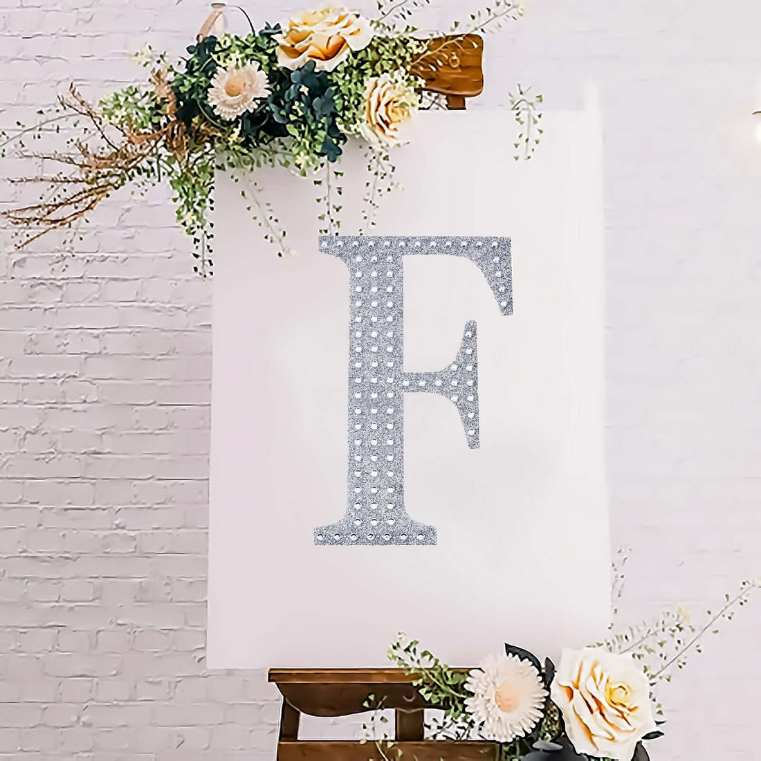 Glittery letter F on a white canvas with floral accents.