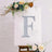 Glittery letter F on a white canvas with floral accents.