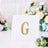 Gold glitter letter "G" on a white card with floral background.