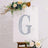 Glittery letter G on a decorative backdrop with flowers and greenery.