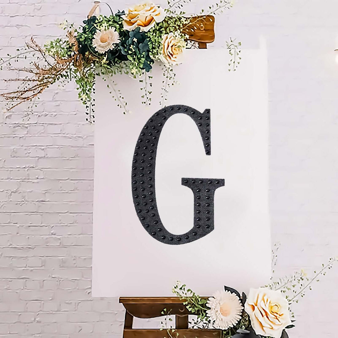 Decorative letter "G" displayed on an easel with floral accents.
