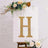 Gold marquee letter "H" adorned with flowers on an easel backdrop.
