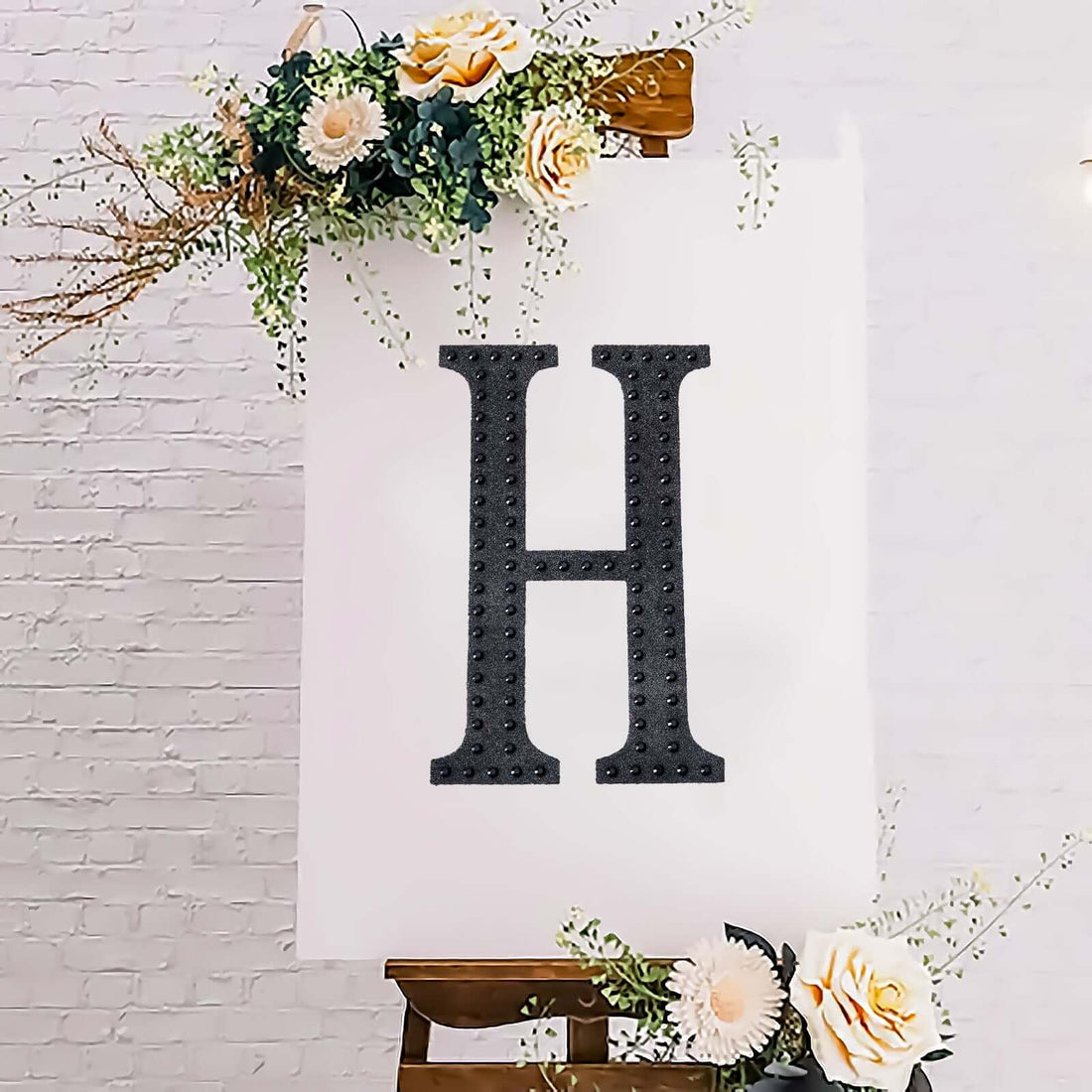 Decorative letter "H" on an easel with floral accents.