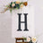 Decorative letter "H" on an easel with floral accents.
