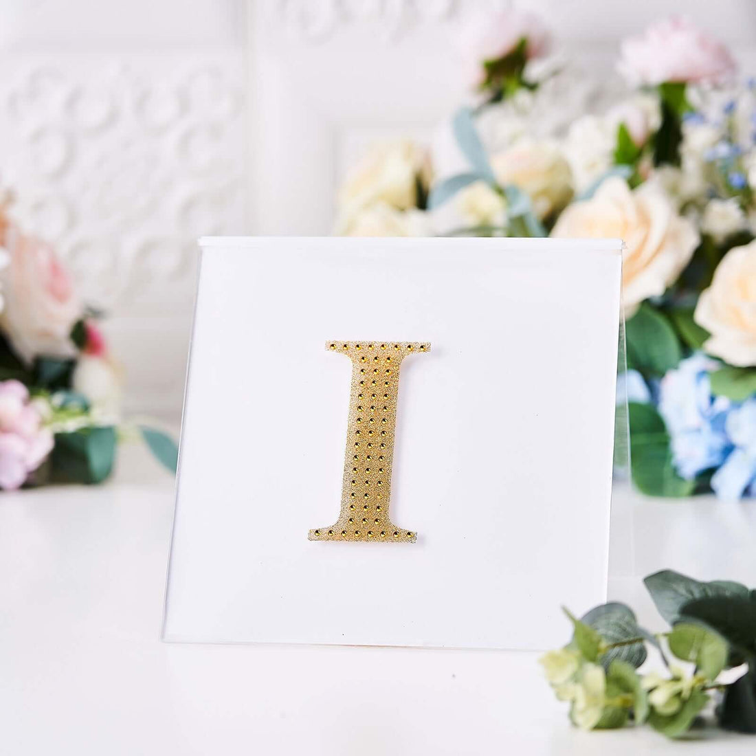 Gold rhinestone letter "I" on a white background.