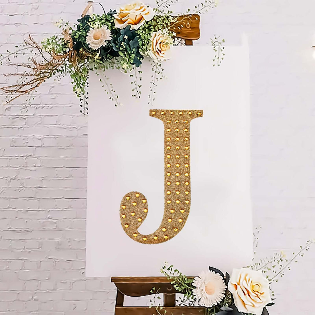 Glittery gold letter J on a decorated easel with floral accents.