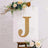 Glittery gold letter J on a decorated easel with floral accents.