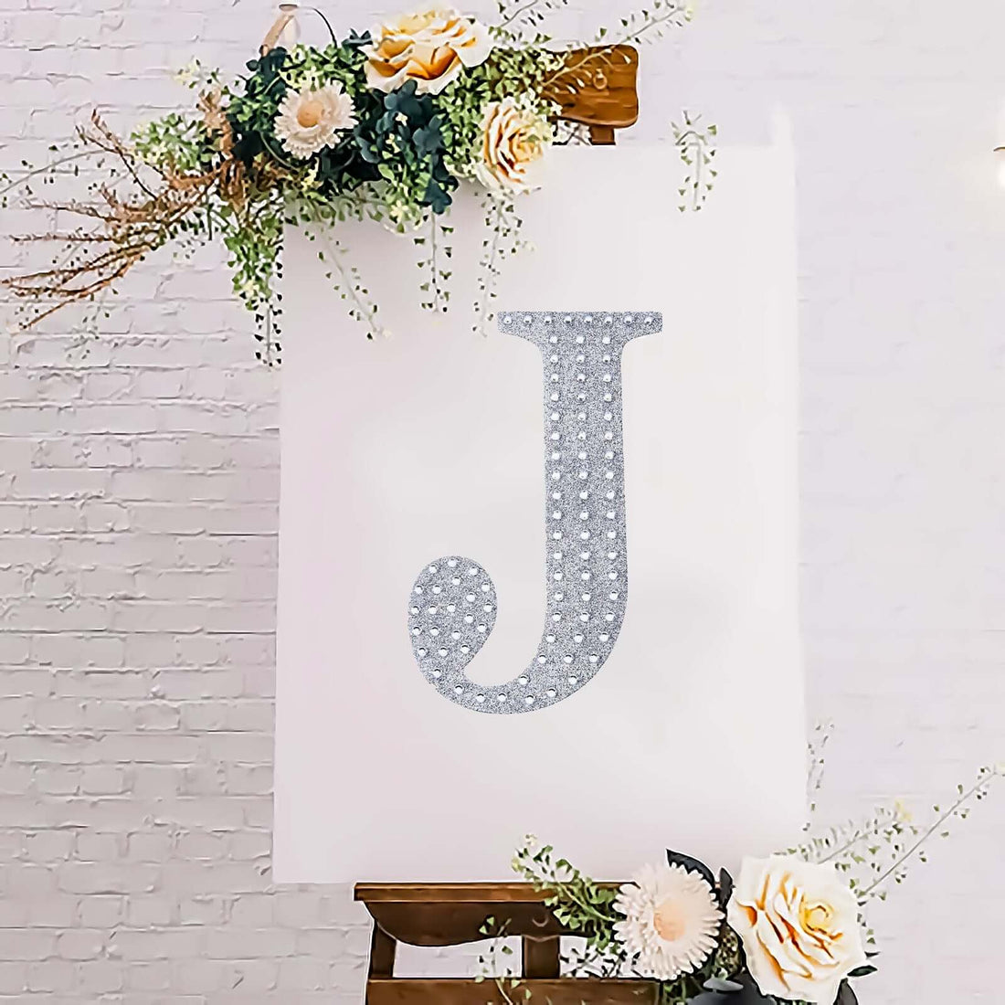 Decorative letter "J" with glitter on a canvas surrounded by flowers.