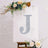 Decorative letter "J" with glitter on a canvas surrounded by flowers.