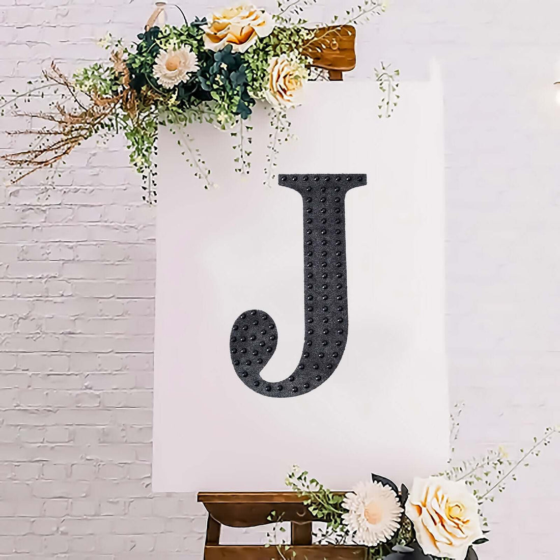 Decorative letter "J" on an easel with floral accents.
