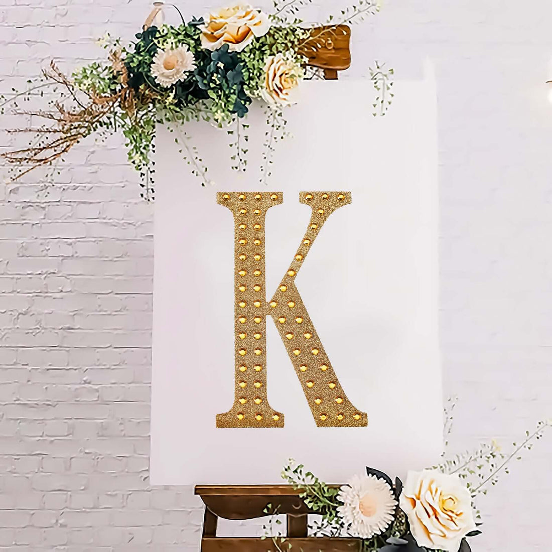 Glittery gold letter "K" on a white canvas with floral accents