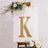Glittery gold letter "K" on a white canvas with floral accents