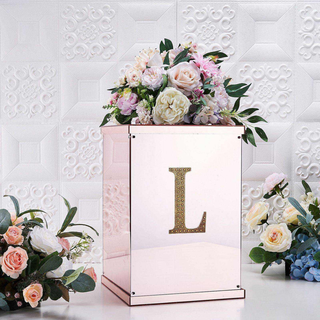 Rose gold flower box with initial "L" and floral arrangement on a decorative background.
