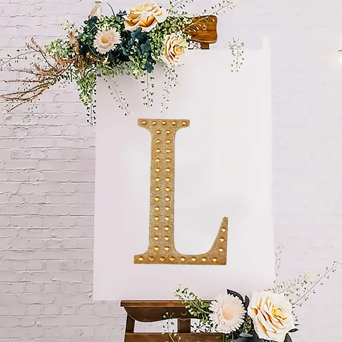 Gold marquee letter "L" decorated with flowers on an easel.