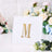 Gold rhinestone letter "M" on a white card with floral background.