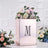 Decorative floral arrangement in a mirrored box with initial 'M' on a textured background.