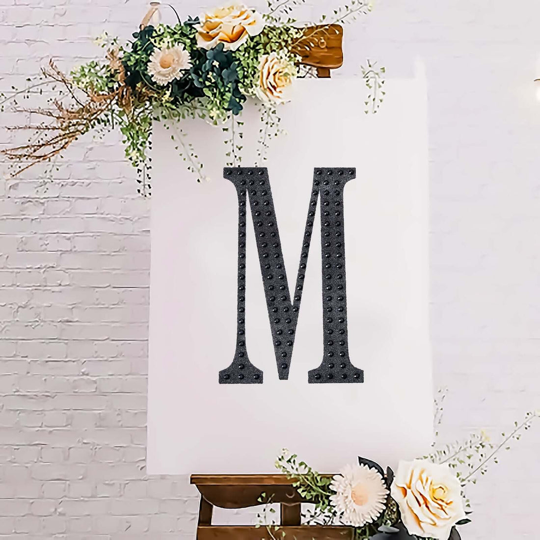 Decorative letter "M" on an easel with flowers, styled for events or decor.