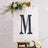 Decorative letter "M" on an easel with flowers, styled for events or decor.
