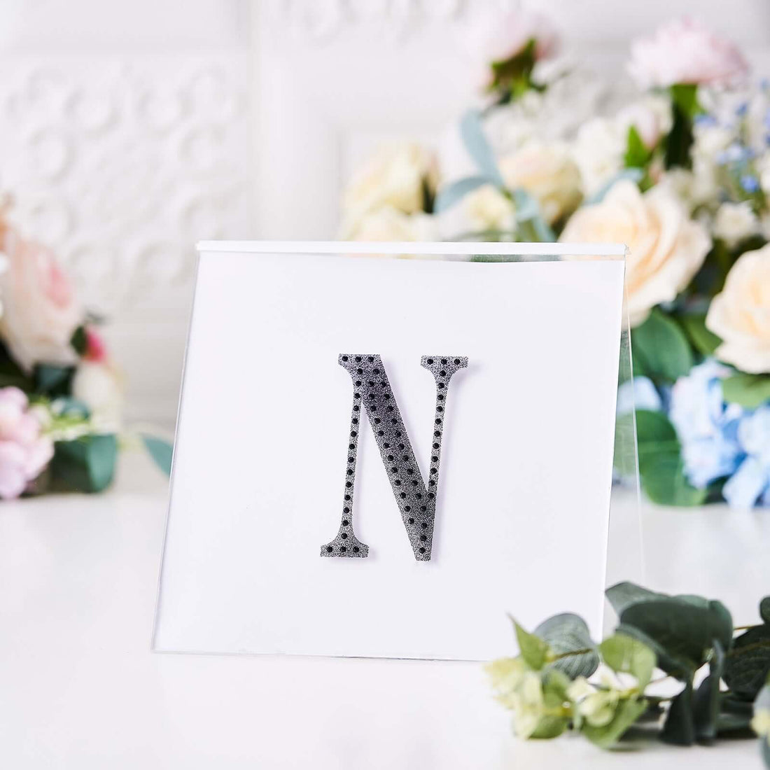 Decorative letter "N" in silver with rhinestones on a clear stand.