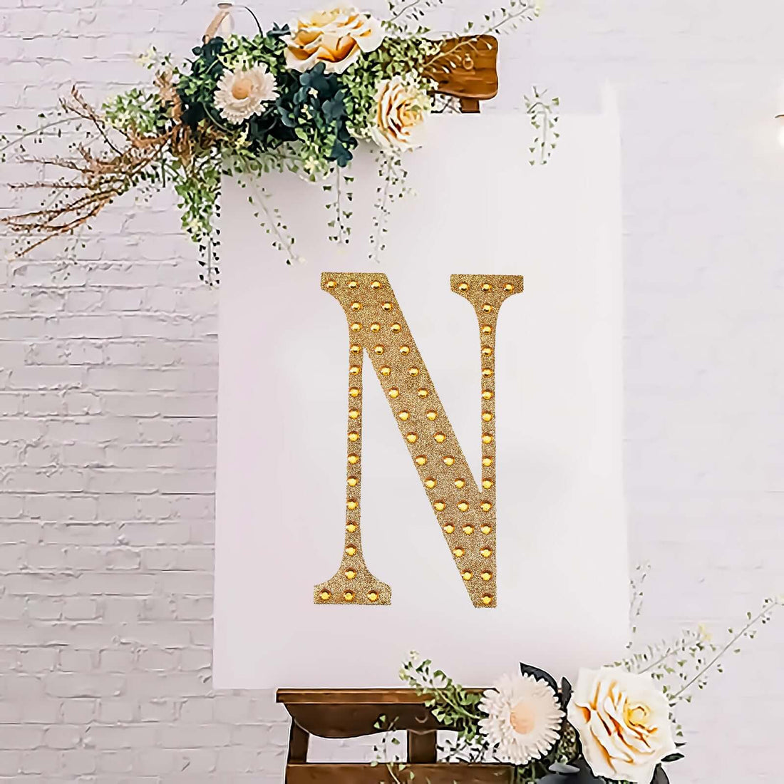 Gold studded letter "N" on a decorative canvas with flowers.