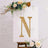Gold studded letter "N" on a decorative canvas with flowers.